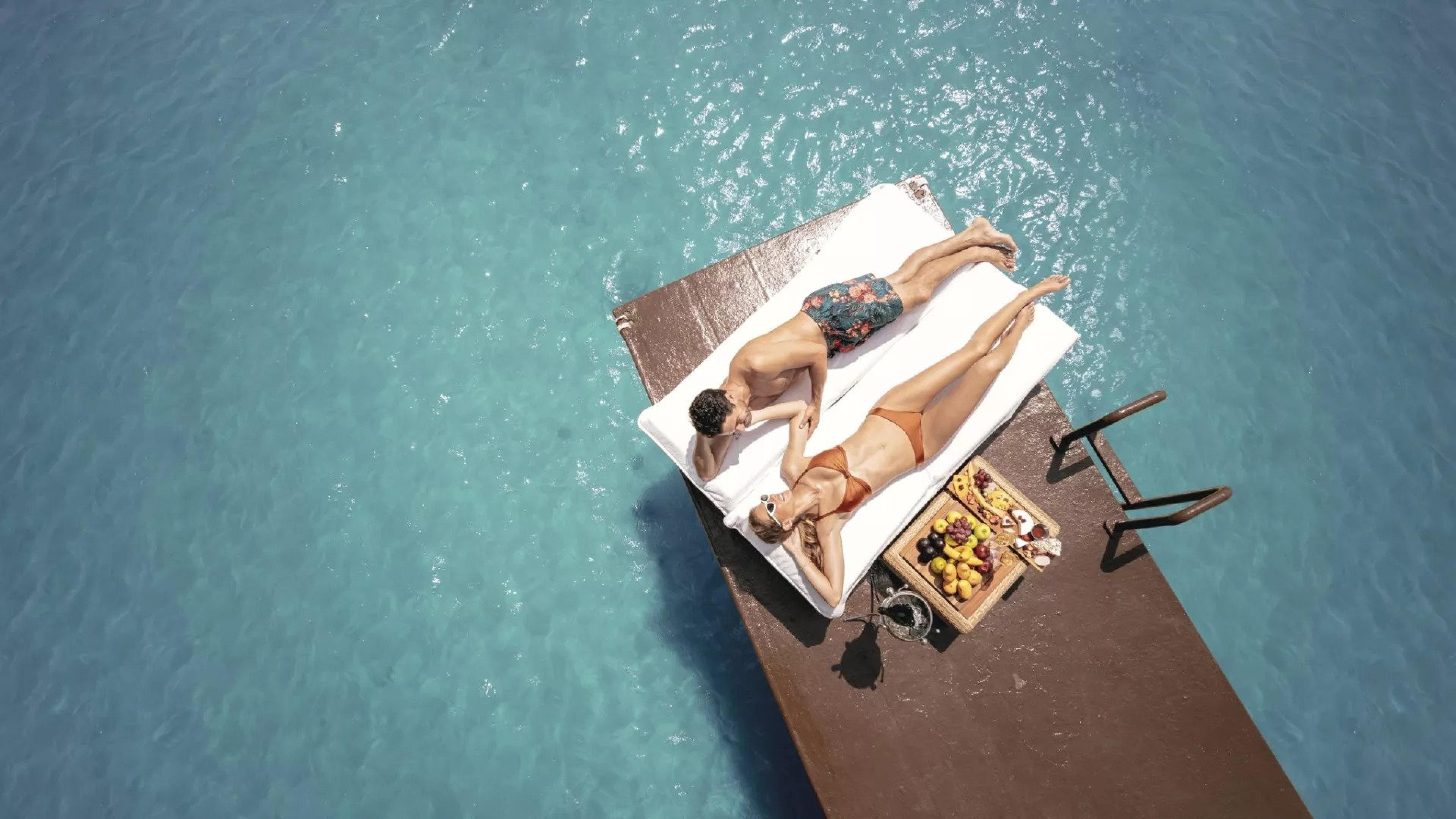 Two people laying on a towel by the water